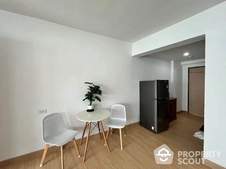 Modern minimalist dining area with table, chairs, and potted plant in a bright apartment.