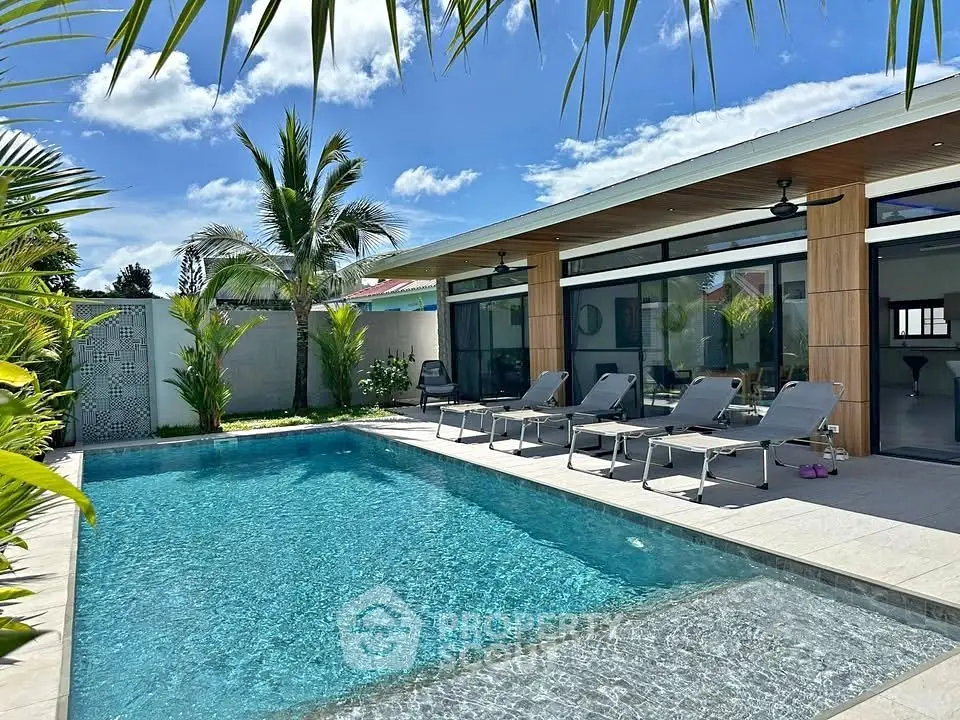 Luxurious modern villa with private pool and sun loungers, surrounded by tropical greenery.