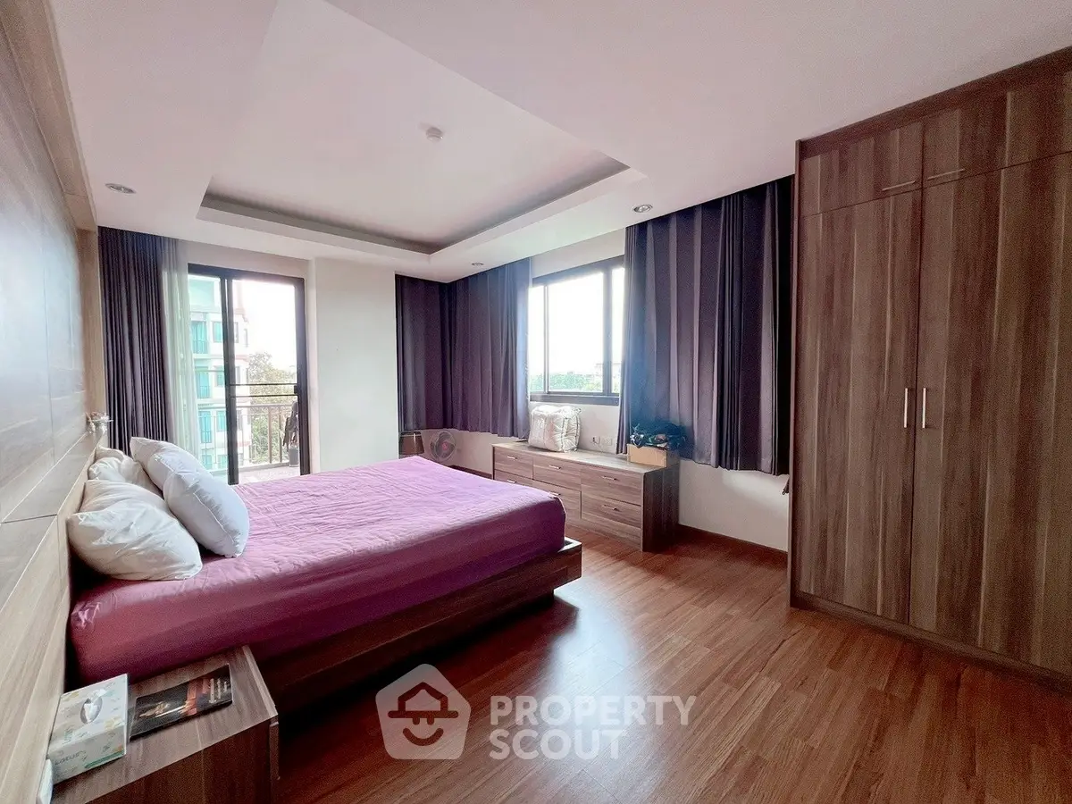 Spacious bedroom with modern wooden flooring and large windows offering natural light.