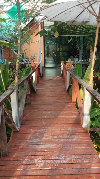 Charming wooden bridge leading to a tropical garden entrance with lush greenery and rustic decor.