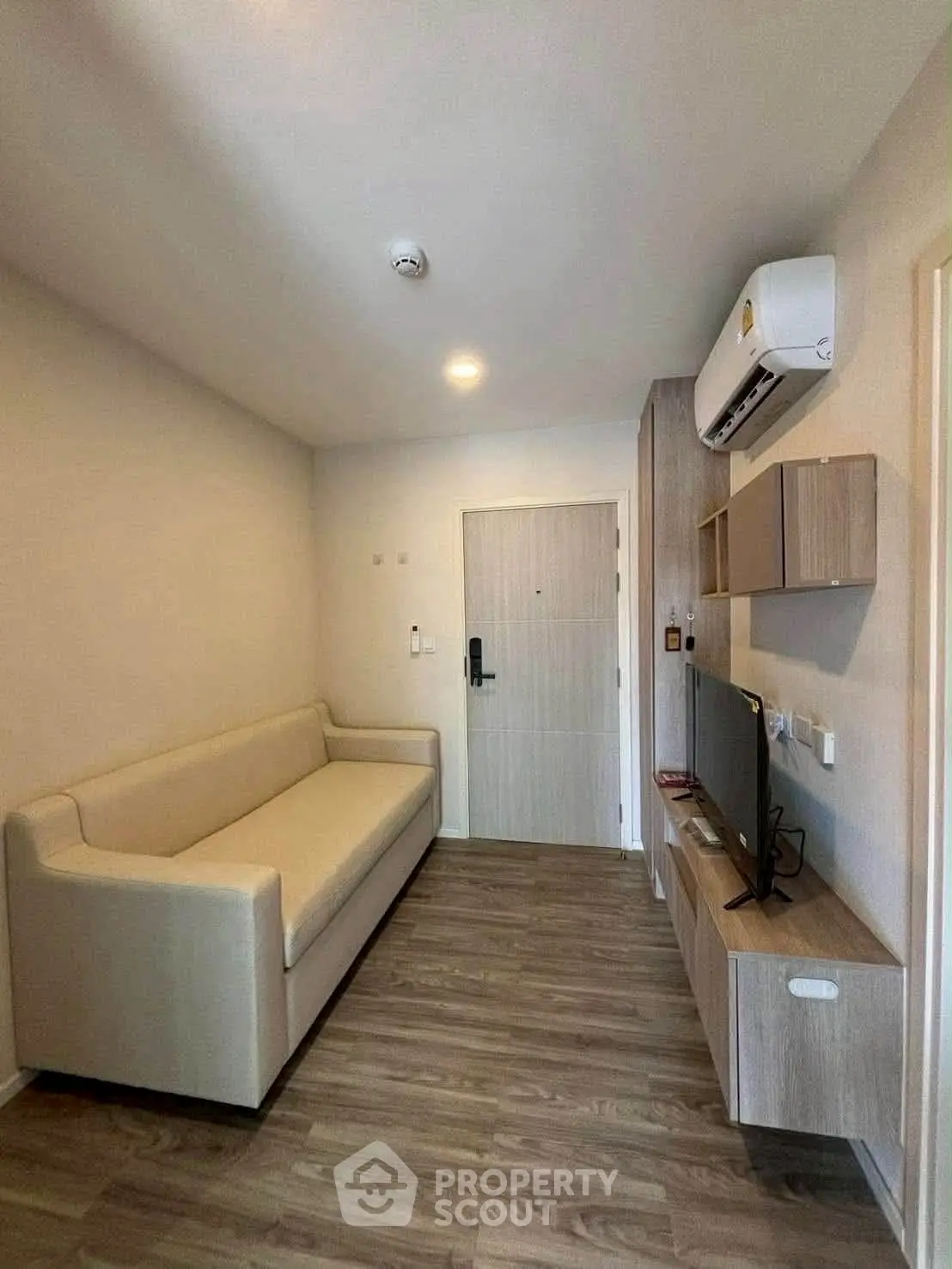 Modern living room with sleek furniture and wooden flooring, featuring a cozy sofa and wall-mounted TV.