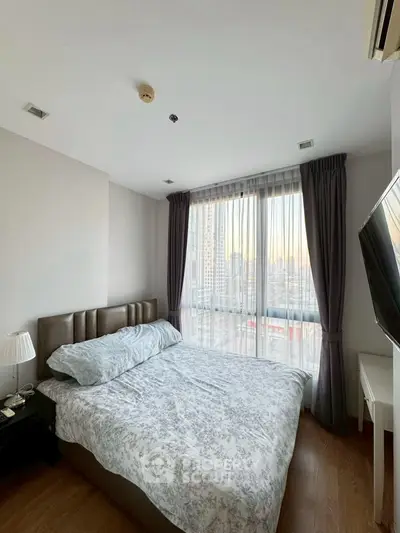 Cozy bedroom with large window and city view, featuring stylish decor and natural light.