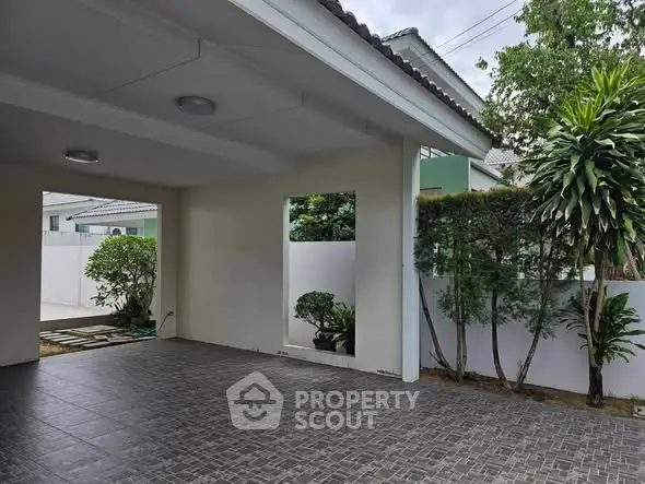 Spacious covered parking area with tiled flooring and lush greenery.