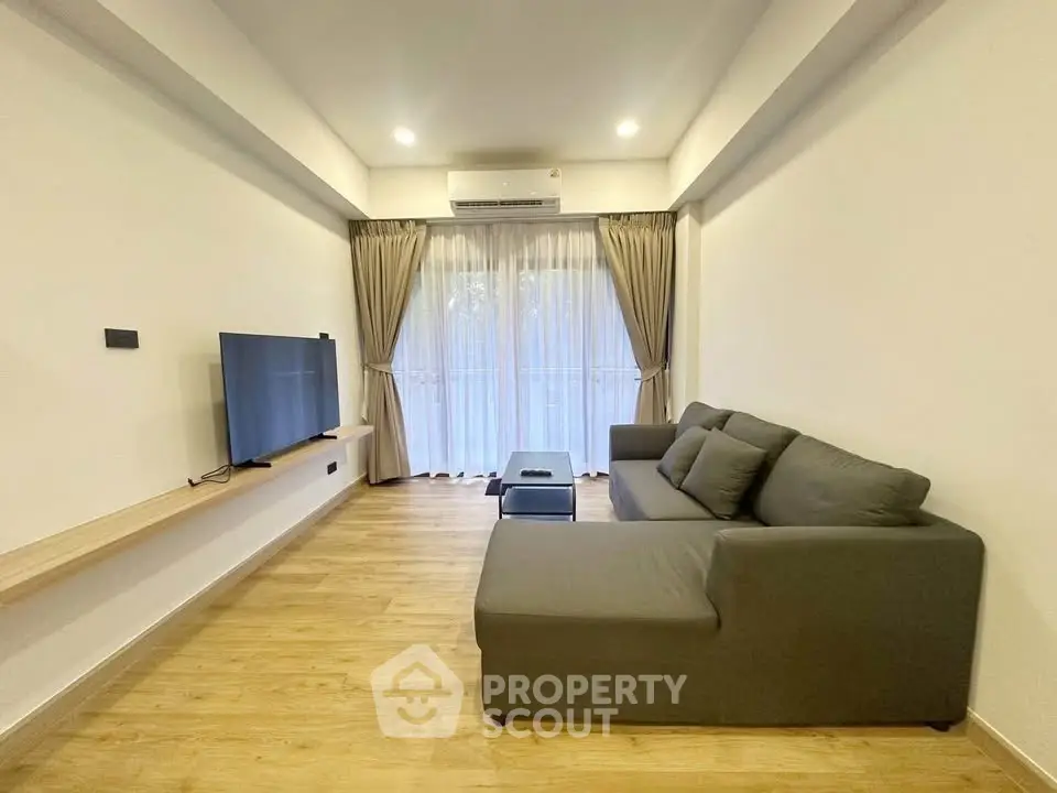 Modern living room with sleek sofa and wall-mounted TV, featuring elegant curtains and warm wooden flooring.