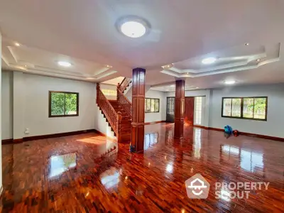 Spacious open living area with polished wooden floors and elegant staircase