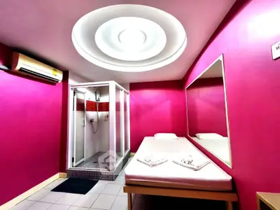 Vibrant pink room with modern shower and minimalist bed setup, ideal for unique living experience.