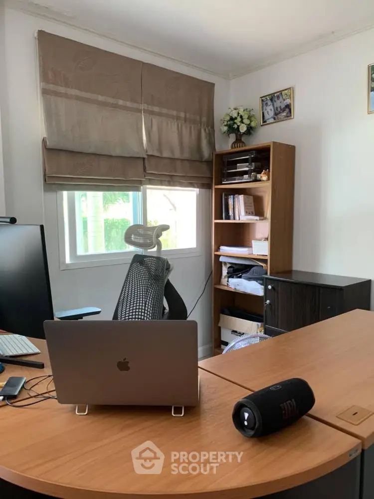 Modern home office with desk, laptop, and bookshelf in bright room.