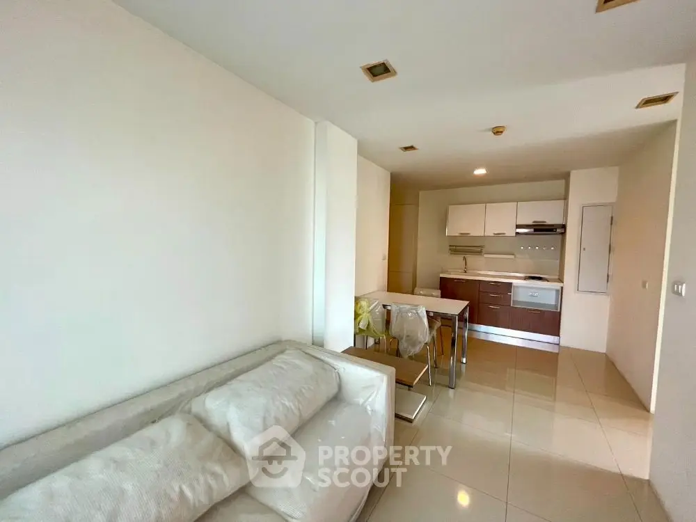 Modern open-layout living room and kitchen with sleek furniture and tiled flooring.