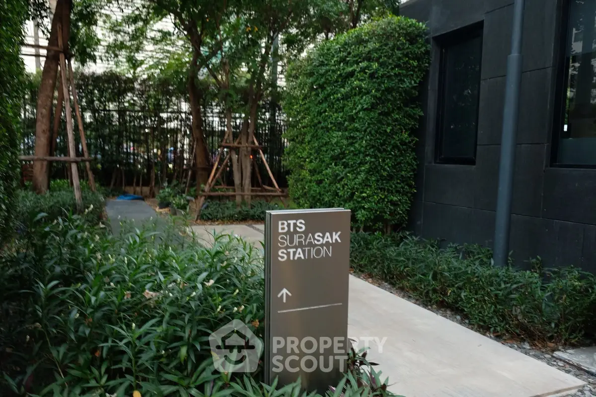 Modern garden pathway leading to BTS Surasak Station, surrounded by lush greenery.