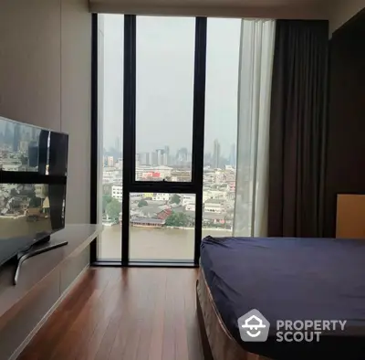 Spacious bedroom with floor-to-ceiling windows offering panoramic city views, sleek wooden flooring, and modern furnishings.