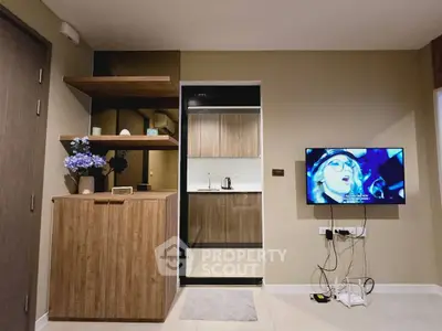 Modern living room with stylish wooden cabinetry and mounted TV, adjacent to a sleek kitchen area.