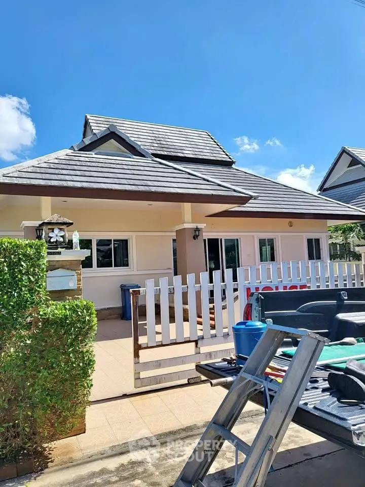 Charming single-story house with a tiled roof and fenced yard under a clear blue sky.