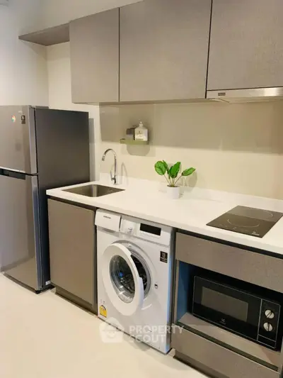 Modern kitchen with sleek appliances including fridge, washing machine, and microwave in a compact layout.