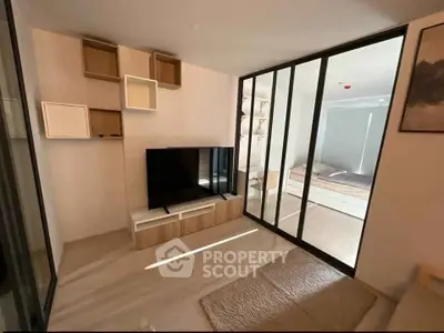Modern living room with sleek TV unit and sliding glass doors leading to a cozy bedroom.