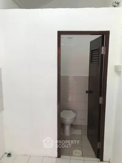 Compact bathroom with white tiles and a wooden door, ideal for minimalist design enthusiasts.