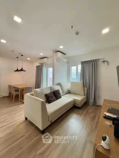 Modern living room with cozy sofa and dining area, featuring wooden flooring and natural light.