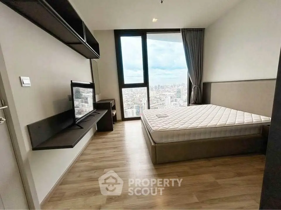 Modern bedroom with city view, featuring sleek furniture and large window.
