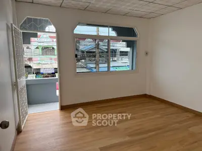 Spacious empty room with wooden flooring and large window offering street view.
