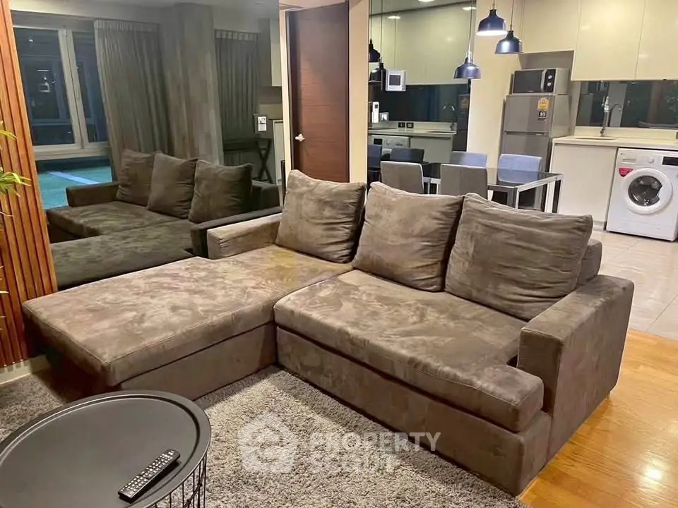 Modern living room with plush sectional sofa and open kitchen featuring dining area and washing machine.