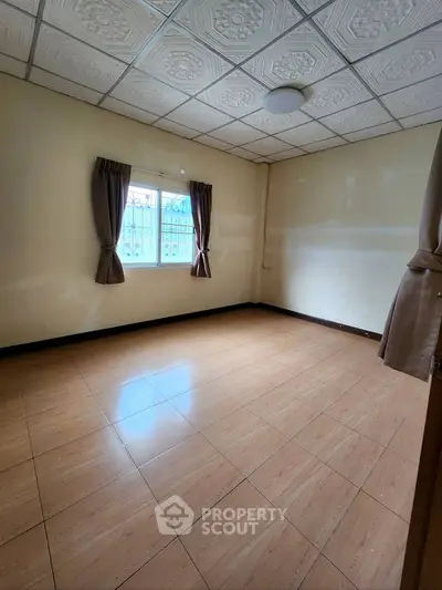 Spacious empty room with tiled floor and window, ideal for customization.