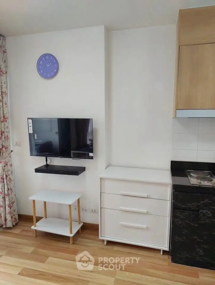 Modern living room with wall-mounted TV, stylish furniture, and sleek kitchen area.