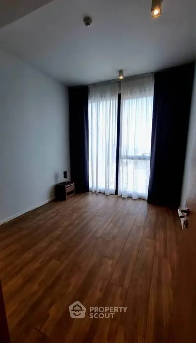 Spacious empty room with wooden flooring and large windows offering natural light.