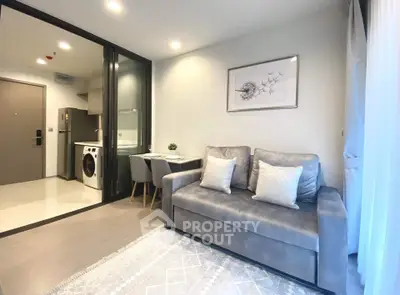 Modern living room with stylish sofa, dining area, and kitchen featuring a washing machine.