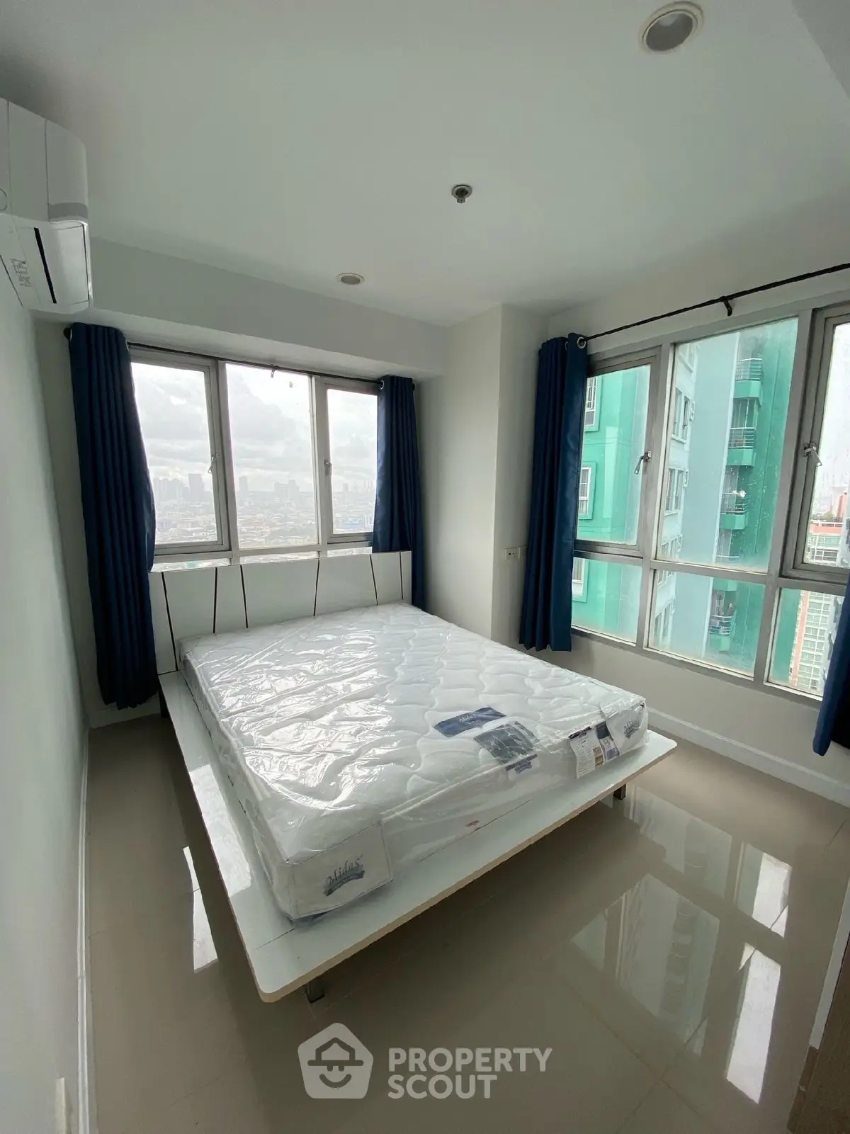 Bright bedroom with large windows offering city views, featuring a modern bed and air conditioning.