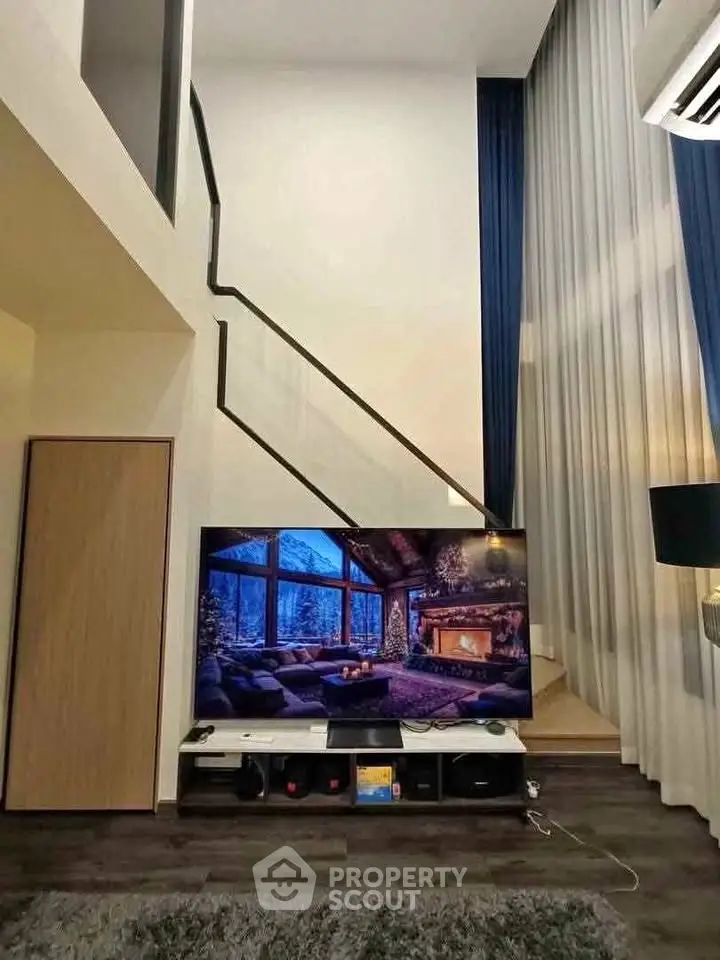 Modern living room with high ceilings and stylish decor, featuring a large TV and elegant staircase.