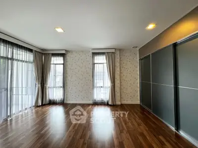 Spacious empty room with elegant wooden flooring and large windows for natural light.