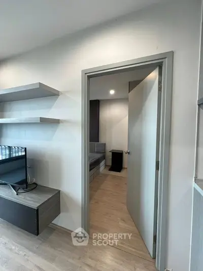 Modern apartment interior with sleek shelves and TV unit, leading to a cozy bedroom.