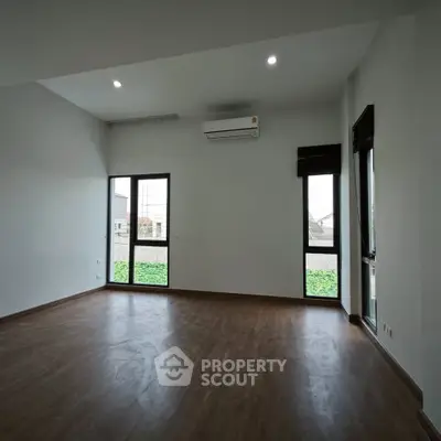 Spacious empty room with wooden flooring and large windows, perfect for customization.