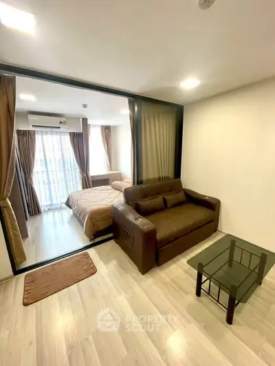 Modern apartment interior with cozy living room and bedroom separated by glass doors, featuring stylish furniture.