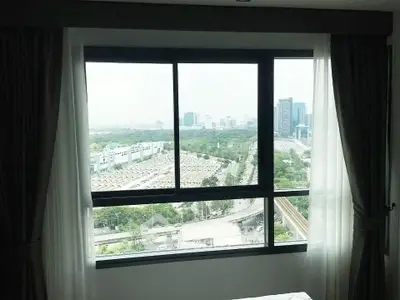 Stunning cityscape view from high-rise apartment window with lush greenery and urban skyline.