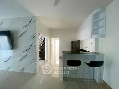 Modern open-plan kitchen with sleek bar stools and marble accent wall
