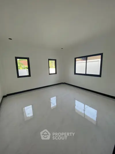 Spacious empty room with glossy white tile flooring and large windows for natural light.