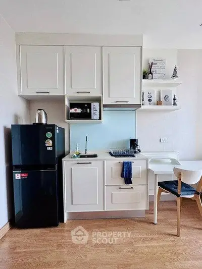 Modern compact kitchen with sleek white cabinets and black fridge in cozy apartment.