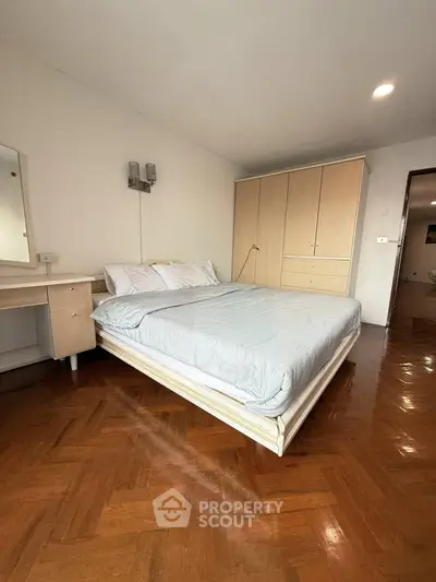 Spacious bedroom with wooden flooring and modern furniture in a stylish apartment.