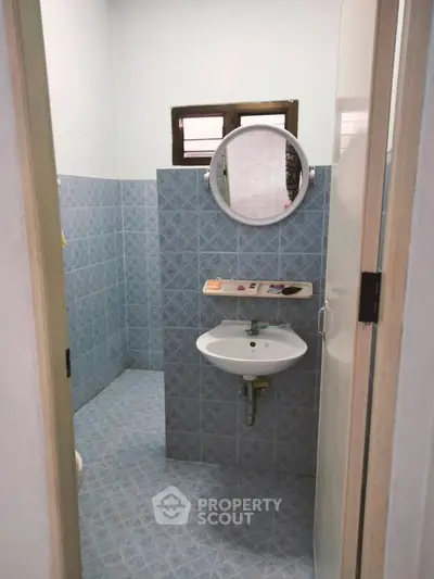 Compact bathroom with blue tile walls and a round mirror above a white sink.