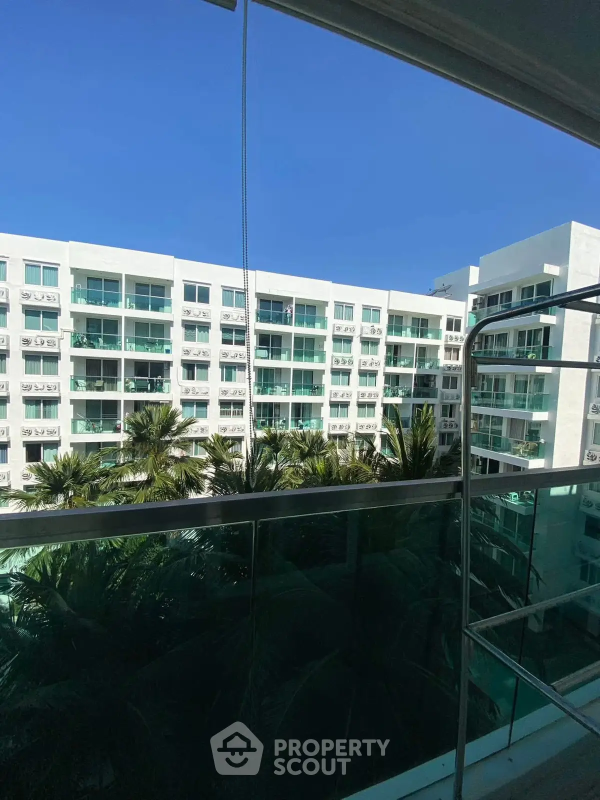 Modern apartment building with glass balconies and lush palm trees under clear blue sky.