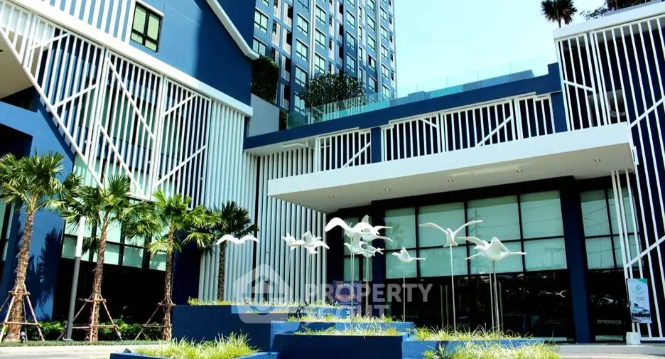 Modern blue and white building exterior with artistic bird sculptures and lush greenery.