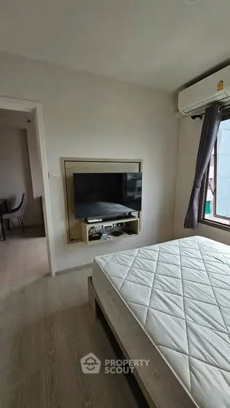 Modern bedroom with wall-mounted TV and air conditioning, featuring a minimalist design and natural light.
