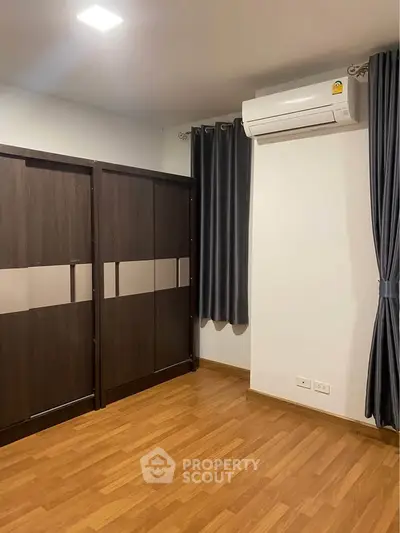 Modern bedroom with wooden flooring and built-in wardrobe, featuring sleek air conditioning unit.