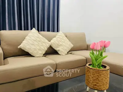 Cozy living room with beige sofa and decorative pillows, complemented by a glass coffee table with pink tulips.