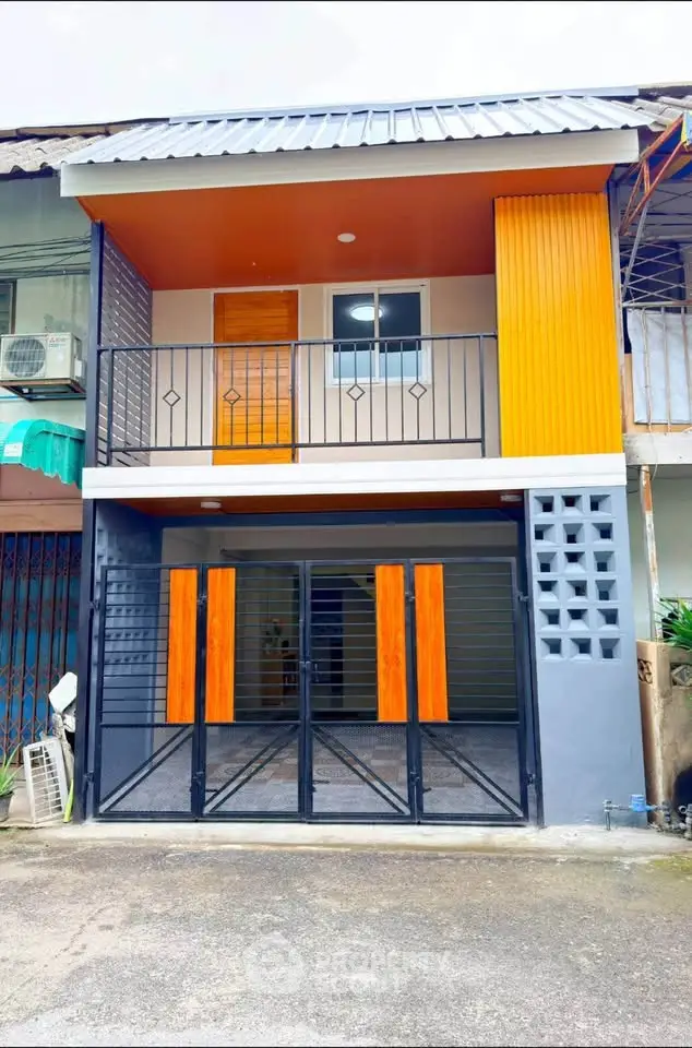 Modern two-story townhouse with vibrant orange accents and sleek black gate.