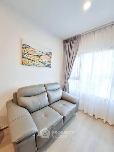 Modern living room with stylish gray sofa and scenic artwork, featuring elegant curtains and natural light.