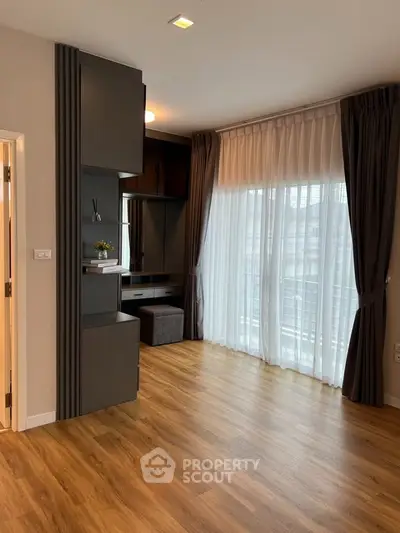 Spacious modern living room with elegant wooden flooring and large window draped with sheer curtains.