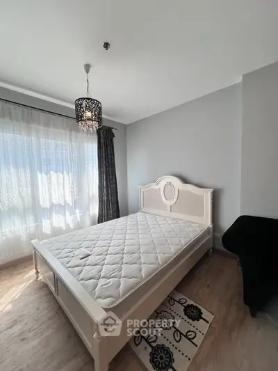 Bright bedroom with elegant bed and chandelier, featuring large window and stylish decor.