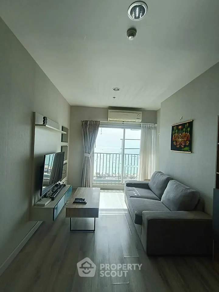 Modern living room with large window and sea view, featuring a cozy sofa and entertainment center.