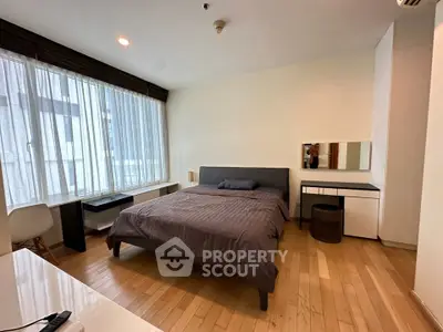 Spacious modern bedroom with large windows and wooden flooring in a stylish apartment.